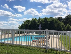 Una piscina amb una tanca blanca, rodejada de cadires i ombrel·les, sota un cel amb núvols dispersos.