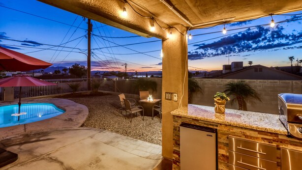 A patio area with a pool, outdoor seating, and a bar with stainless steel appliances.