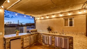 A kitchen with a stone backsplash, stainless steel appliances, and a view of the ocean at dusk.