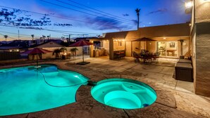 A backyard with a swimming pool, hot tub, and outdoor dining area.