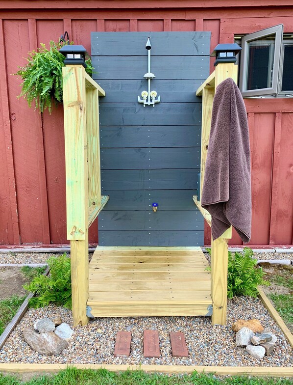 A wooden deck with a black backdrop, a towel hanging on the right, and a small plant on the left.