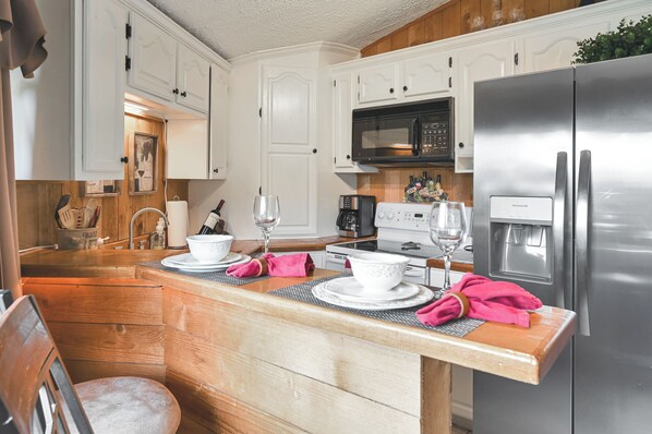 A kitchen with white cabinets, a stainless steel refrigerator, a microwave, and a wooden island with a sink.