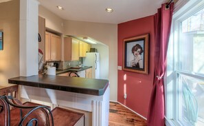 A kitchen with a wooden countertop, a refrigerator, and a microwave. There is a window with red curtains and a framed picture on the wall.