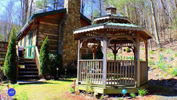 A rustic cabin with a stone chimney, a wooden deck, and a gazebo.