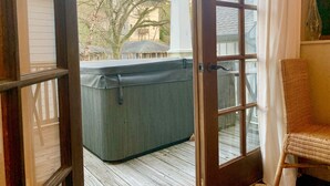 A covered outdoor area with a hot tub, wooden deck, and a wicker chair. - Stunning contemporary North Shore Bungalow with hot tub. Steps to everything.  (Chattanooga)