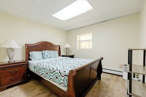 Un dormitorio con cama de madera, dos mesitas de noche con lámparas, una ventana y un radiador.