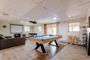 A room with a pool table, a sofa, a projector screen, and a billiards rack.