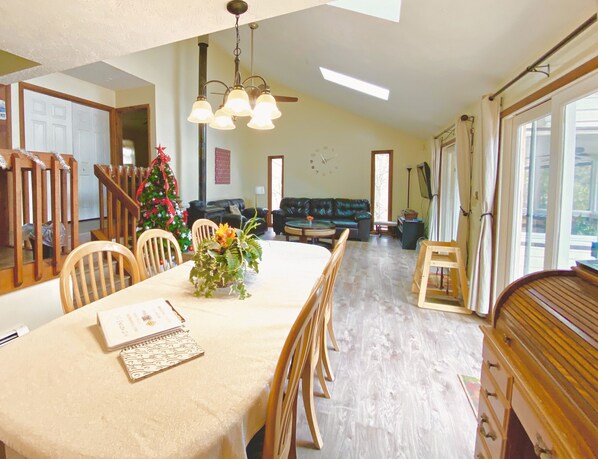 Un comedor con una mesa preparada para cuatro personas, un árbol de Navidad y una sala de estar con un sofá y una televisión.