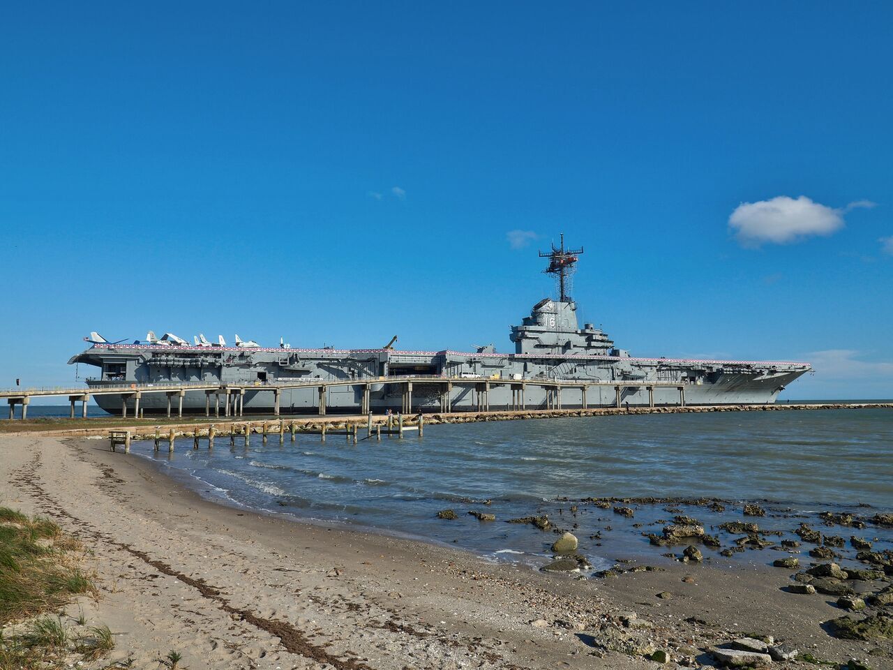 An aircraft carrier docked at a pier with a clear sky.