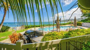 A pool area with lounge chairs and a grill, surrounded by lush greenery and overlooking the ocean. - Lanikai 232 “Seascape” | Ocean View | Central A/C | Sleeps 4 (Kapaa)