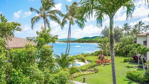 A lush garden with palm trees, a swimming pool, and a view of the ocean. - Lanikai 232 “Seascape” | Ocean View | Central A/C | Sleeps 4 (Kapaa)