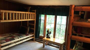 A cabin interior with a bunk bed, a sofa, a table with a lamp, and a window with a view of a forest.