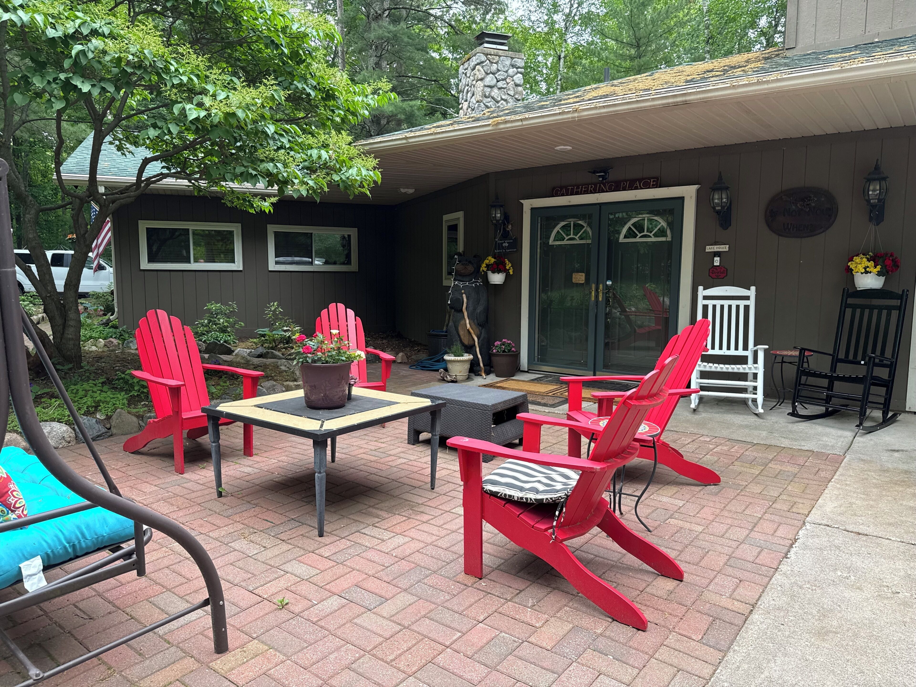 Une terrasse avec des fauteuils Adirondack rouges, une table et un pot de fleurs.