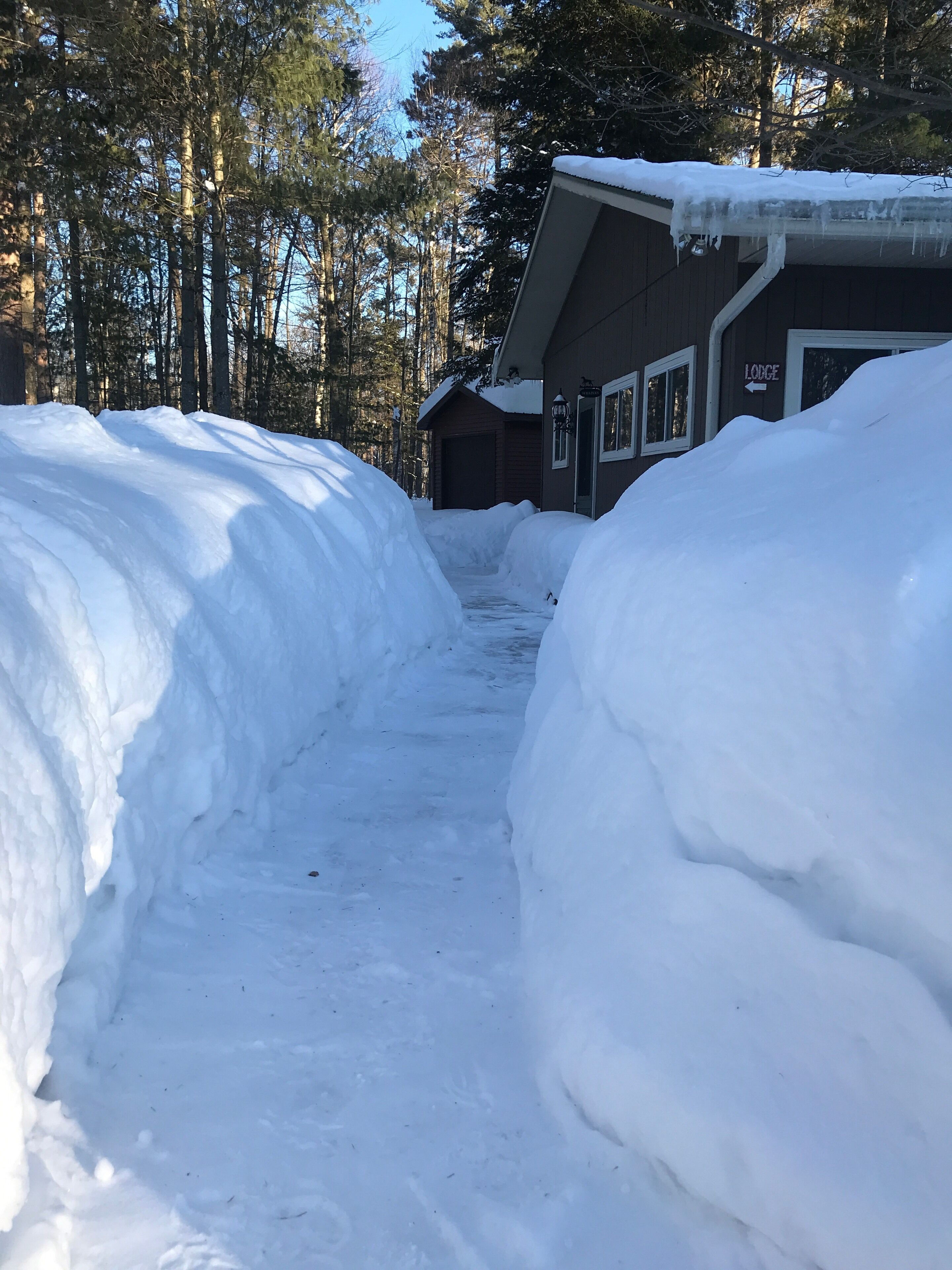 Camino cubierto de nieve que lleva a una cabaña de madera con un letrero con su nombre.
