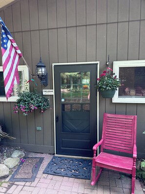 Une façade en bois avec une porte noire, un banc rouge, un drapeau américain suspendu et une enseigne indiquant « THE LODGE ».
