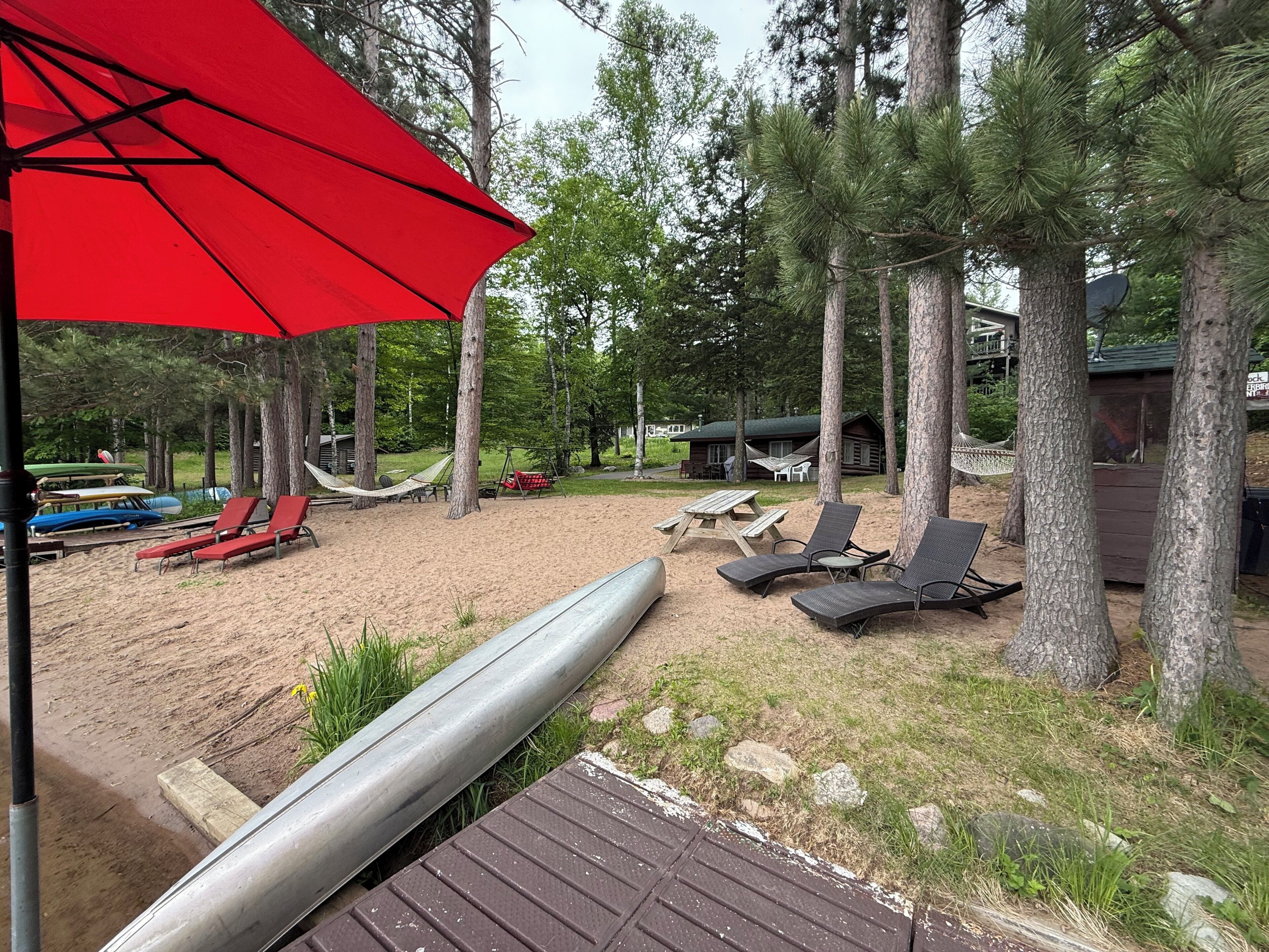 A beach area with lounge chairs, a red umbrella, and a hammock.