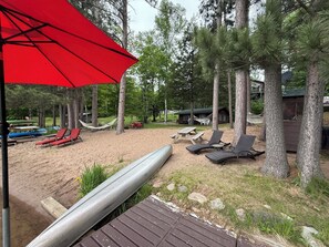 Un espace de plage avec des chaises longues, un parasol rouge et un hamac.
