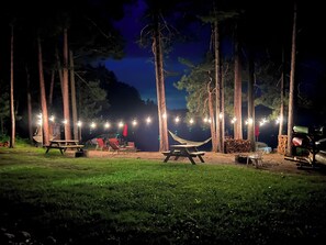 A campsite with picnic tables, a hammock, and string lights. - Thunderbird Lodge: Northwoods Lakefront Retreat— Peak Colors & Pontoon Specials! (Lac du Flambeau)