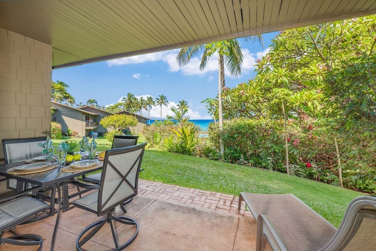 An outdoor patio with a table set for dining, surrounded by lush greenery and a view of the ocean.