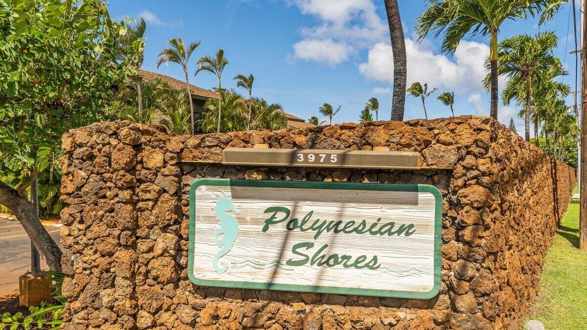 Une enseigne indiquant « Polynesian Shores », avec un mur de pierres et des palmiers en arrière-plan.