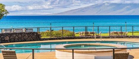 Ein Poolbereich mit Liegestühlen und einer Whirlwanne mit Blick auf einen Strand und einen Berg im Hintergrund.