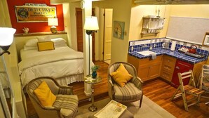 A hotel room with a bed, two armchairs, a small table, a lamp, a kitchen area with blue tiles, and a sign on the wall. - Cozy Studio Apartment with European style (Laguna Beach)