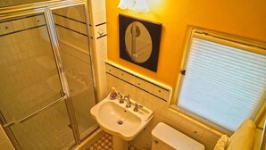 A bathroom with a glass shower enclosure, a pedestal sink, a toilet, and a mirror above the sink. - Cozy Studio Apartment with European style (Laguna Beach)