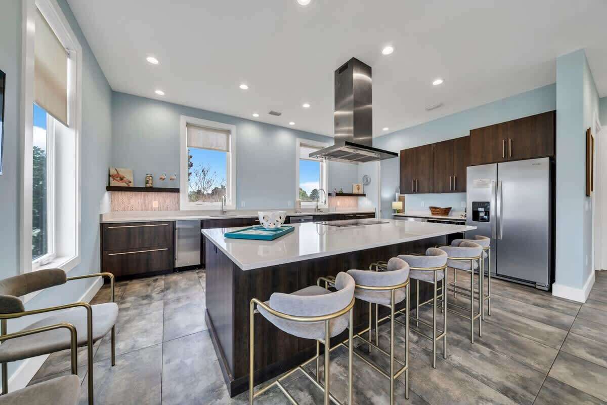 A modern kitchen with a central island, bar stools, stainless steel appliances, and a view of the outdoors.