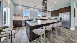 A modern kitchen with a central island, bar stools, stainless steel appliances, and a view of the outdoors.