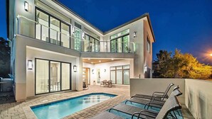 A modern two-story house with a swimming pool, outdoor seating, and large windows.