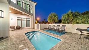 A modern house with a swimming pool, outdoor seating, and a well-lit patio area.