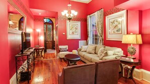 Un salon avec un mur rouge, un lustre, un canapé, une table basse et une table d’appoint avec une lampe.