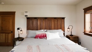 Une chambre à coucher avec une tête de lit en bois, un grand lit recouvert d’une literie blanche et à motifs, deux tables de chevet surmontées de lampes de style lanterne, et une armoire en bois.