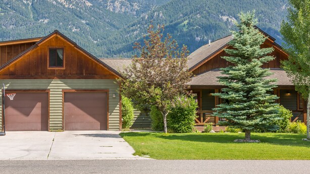 A cabin with a garage, a small yard with a tree, and a mountain backdrop. - Your Base Camp for Big Sky’s Best Runs. Plan your Montana Adventure today! (Big Sky)