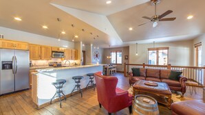 A spacious kitchen with wooden cabinets, a central island with stools, a dining area with a leather sofa, and a wooden barrel. - Your Base Camp for Big Sky’s Best Runs. Plan your Montana Adventure today! (Big Sky)