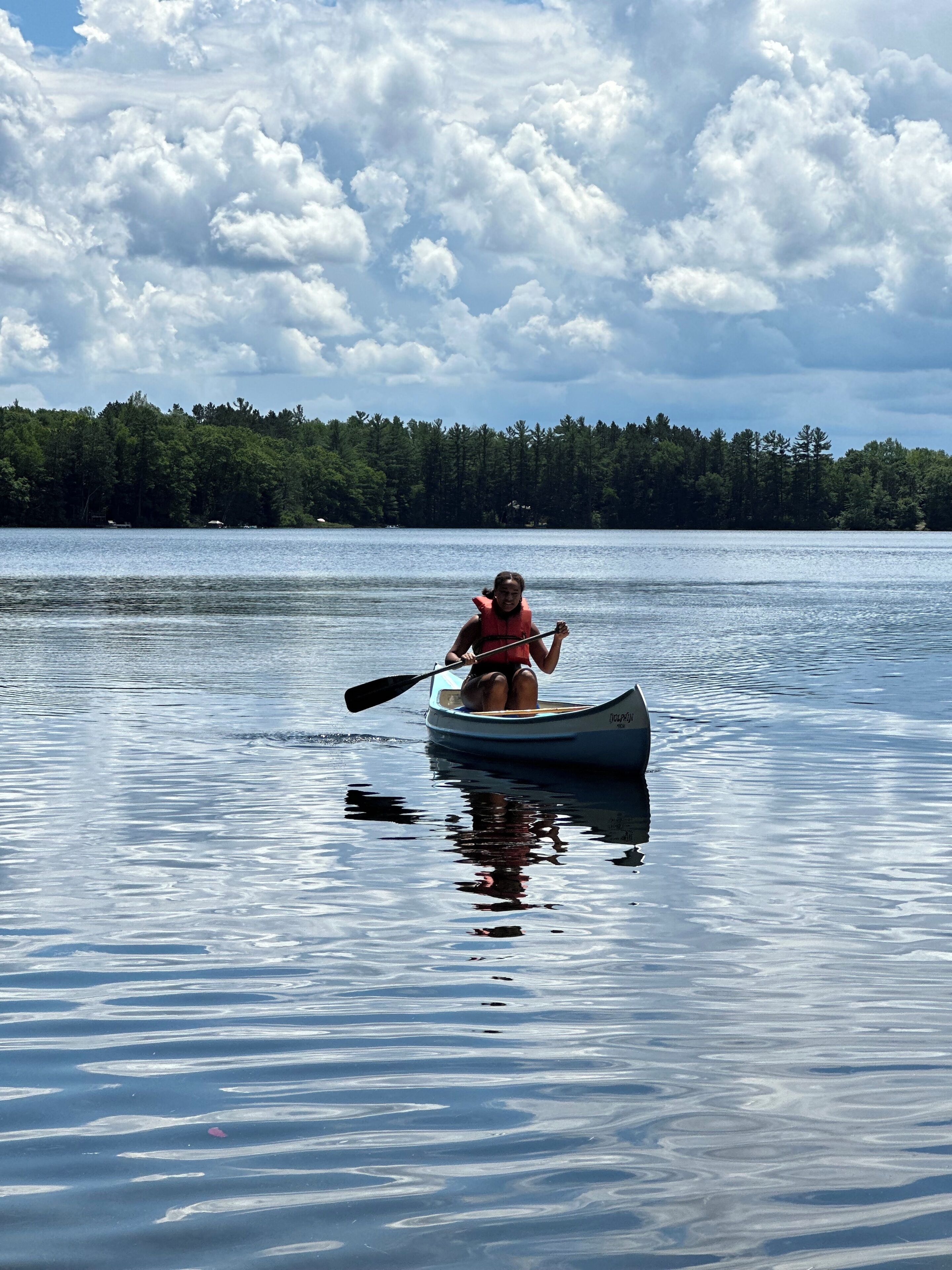 A person in a canoe on a calm lake with a forest in the background.
