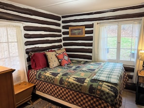 Une chambre à coucher de style chalet, avec une couvre-lit matelassé, une table de chevet en bois et une fenêtre avec des rideaux.