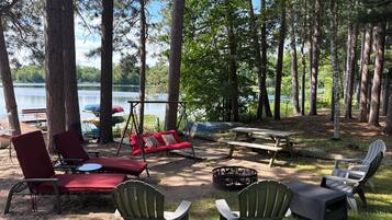 A lakeside campsite with picnic tables, chairs, and a swing.