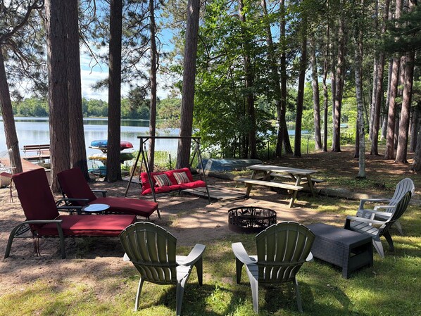A lakeside campsite with picnic tables, chairs, and a swing.