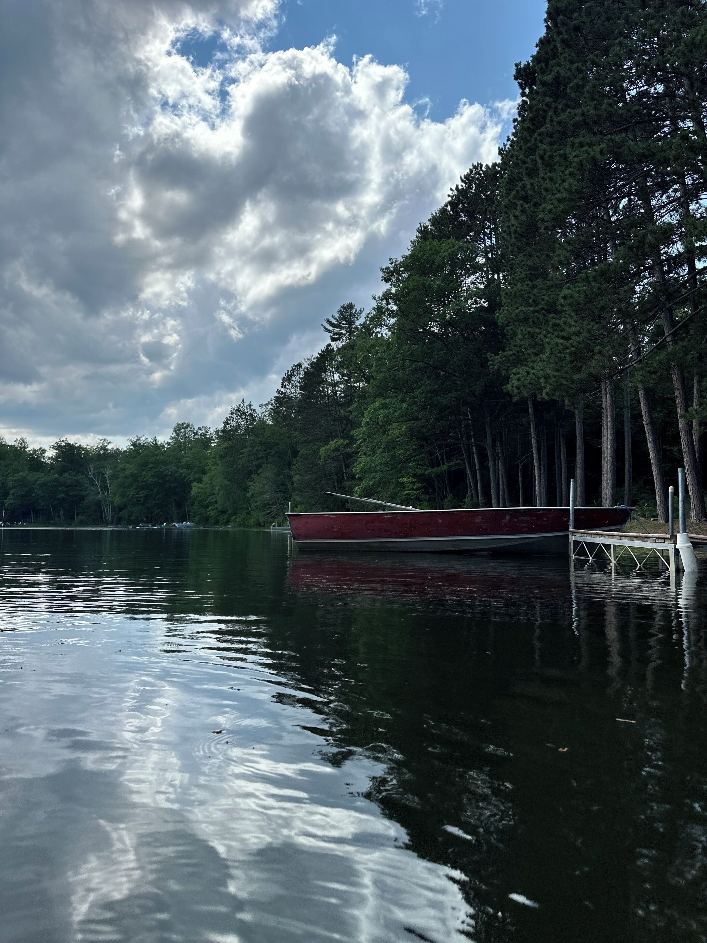 Un lago tranquilo con un bote rojo amarrado en un muelle, rodeado de un bosque denso.