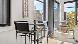 A modern interior with a dining area featuring metal chairs and a table, large windows offering views of the outside, and a decorative wall piece. - Luxurious Downtown-2 bed 2 bath Corner 2M (Nashville)
