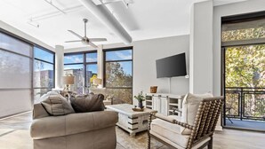 A spacious living room with a sofa, armchair, and coffee table, large windows, and a flat-screen TV mounted on the wall. - Luxurious Downtown-2 bed 2 bath Corner 2M (Nashville)