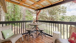 Une terrasse en bois avec une table et des chaises, entourée d’une rambarde, donnant sur une zone boisée.