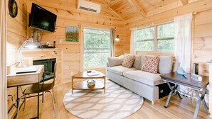 L’intérieur chaleureux d’un chalet avec un plafond en bois, un téléviseur fixé au mur, un canapé, un bureau avec une chaise et une petite table.