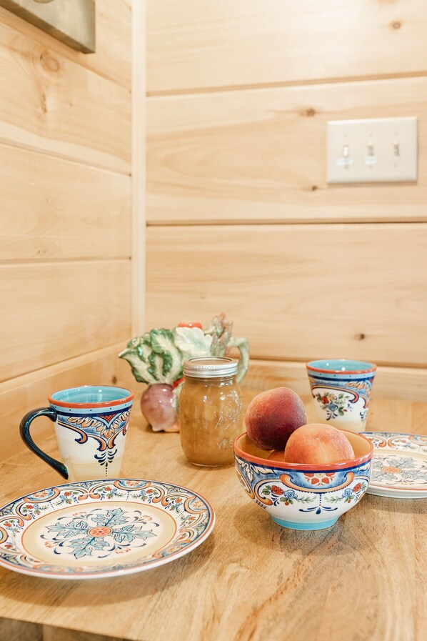 A wooden table with a decorative plate, a ceramic mug, a bowl with fruits, and a jar of honey. - Peaceful, private & serene cabin near wineries, TIEC & outdoor activities (tryon)