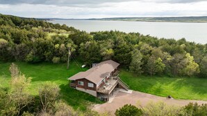 Ein zweistöckiges Haus mit einer Terrasse, umgeben von üppiger Vegetation und einem See.