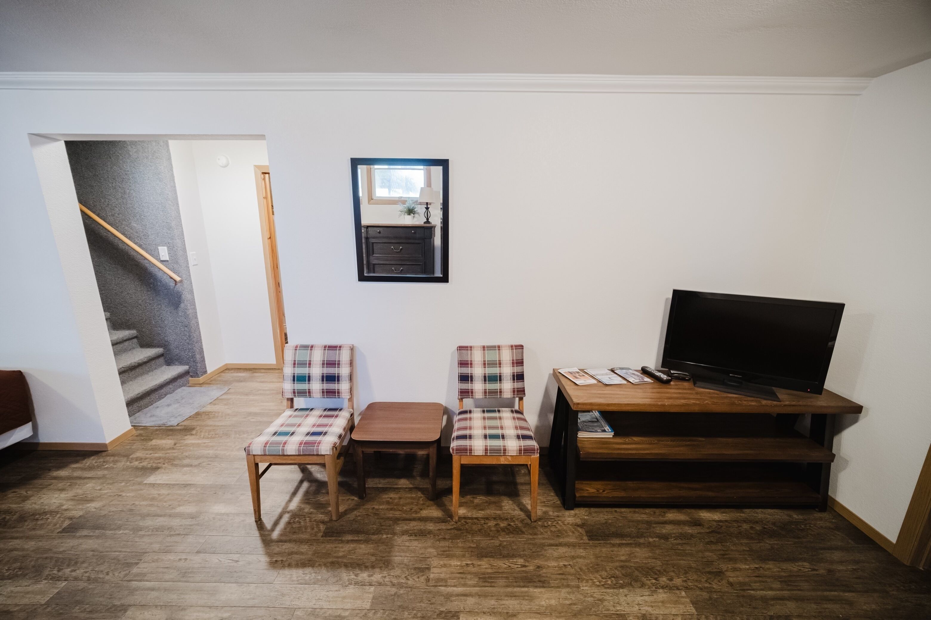 A living room with a wooden floor, a TV on a wooden stand, and two plaid chairs.