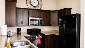 Uma cozinha com armários de madeira escura, eletrodomésticos de aço inoxidável, bancada de granito e um relógio de parede.