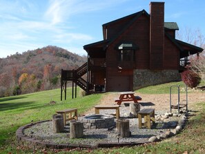 A rustic cabin with a stone foundation, wooden deck, and a fire pit area. - Easy Access w/View, Large Yard, Game Rm, Fire Pit, Hot Tub & Pool Access (Sevierville)