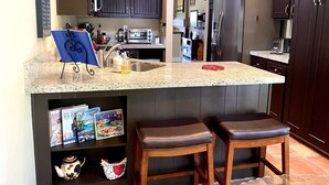 Una cocina con armarios oscuros, encimera de granito, refrigerador de acero inoxidable y horno empotrado.